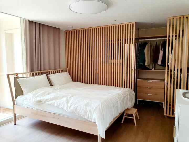A natural wood tone and beige bedroom featuring a wooden bed, curtains, and a closet separated by slatted room dividers, creating a clean, modern space