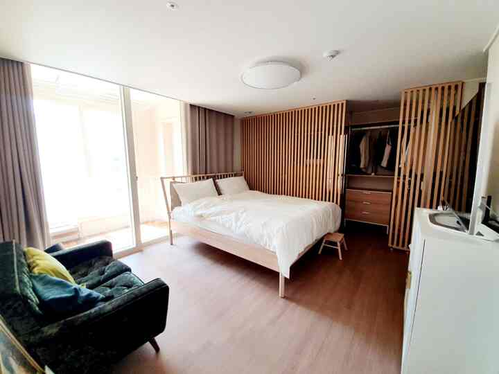 Natural wood tone and white bedroom featuring a deep green sofa and gold handles, creating a cozy atmosphere