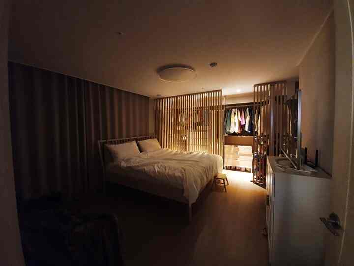 ウッドトーンとホワイトが調和した寝室、木製パーティションとオープンクローゼットが配置された落ち着いた雰囲気のインテリア