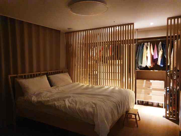 Warm wood tones and white bedding in a bedroom connected to a walk-in closet, softly illuminated by indirect lighting creating a cozy atmosphere