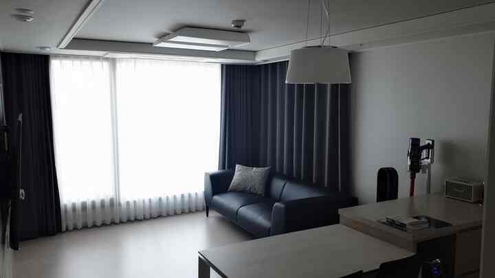 Bright white-toned living room featuring a black leather sofa and dark blackout curtains