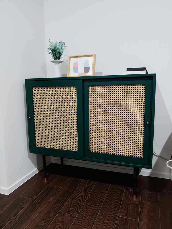 Natural bedroom corner storage featuring a deep green rattan cabinet with wooden floor and decorative elements