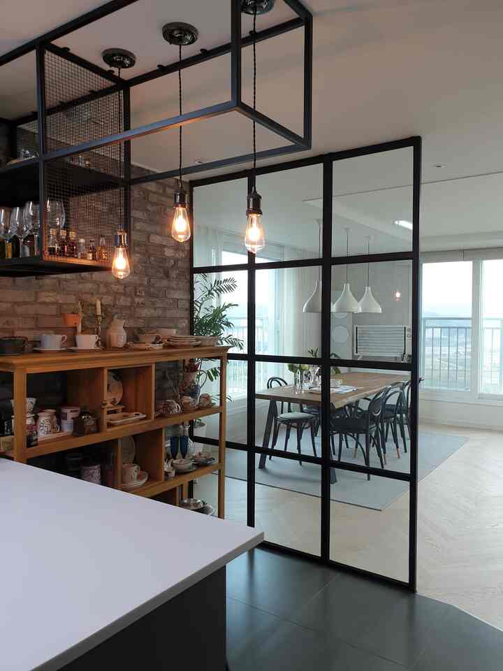 黒い金属パーティションとライトウッド家具が配置されたモダンインダストリアルスタイルのキッチンとリビングスペース