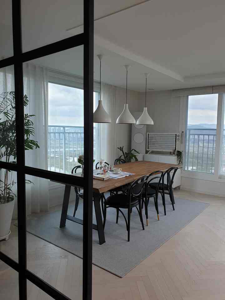 Bright living dining room in white and natural tones featuring a teak table with black dining chairs in a clean setting