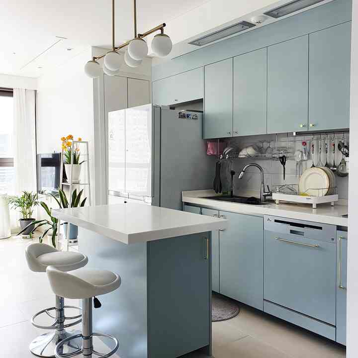 Pastel mint blue and white tone kitchen with a central island, gold handles, and round pendant lights creating a modern clean space