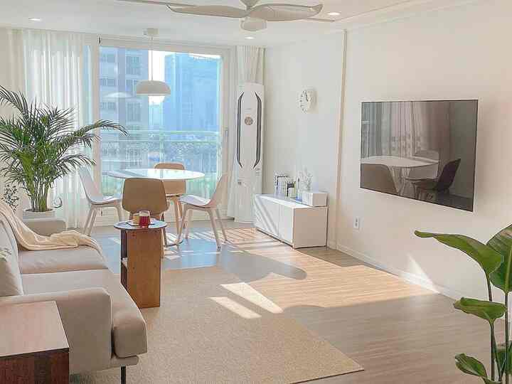 A natural modern living room in white and wood tones featuring a wall-mounted TV and round dining table arranged neatly