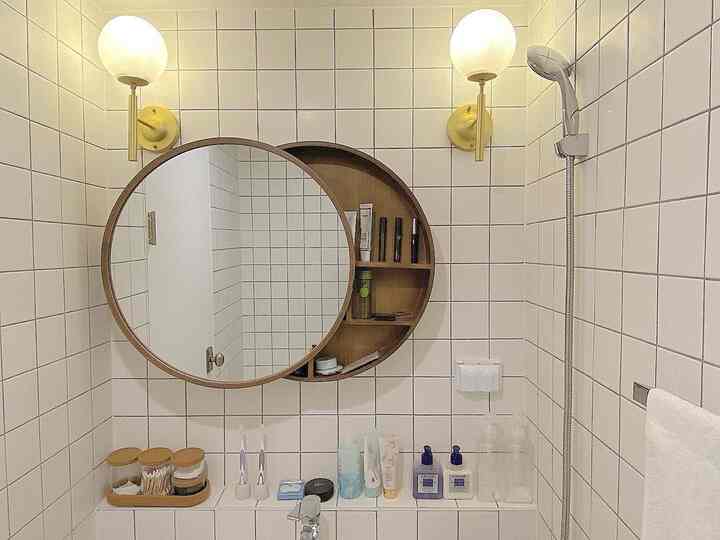 Minimal powder room bathroom with white tiled walls and a wood-tone round mirror