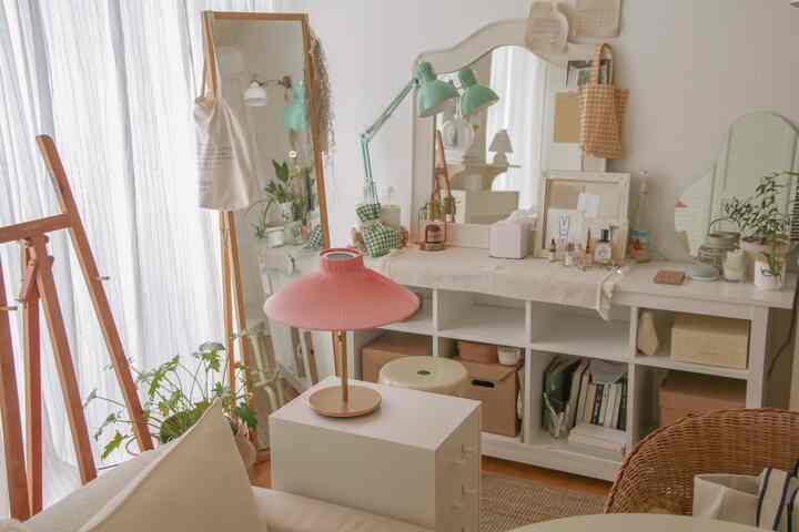 A cozy small room in white and natural tones featuring a vanity with mirrors and a pink table lamp