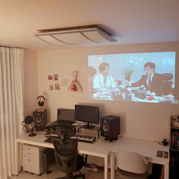 白を基調としたホームオフィス兼ホームシネマの空間、大きなデスクと音響機器が配置されたシンプルでモダンな作業スペース