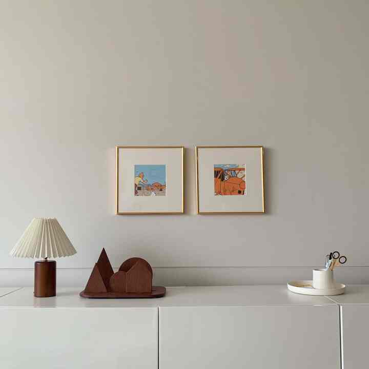 クリームホワイトと木目調のリビングキャビネットの上に金色の額縁が掛けられたシンプルでモダンなインテリア空間