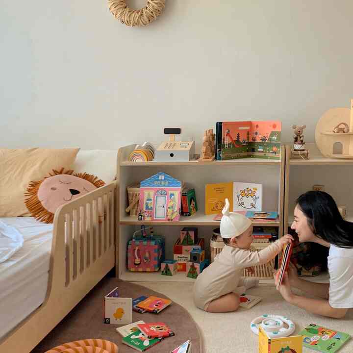 ナチュラルカラーとベージュの子供部屋、ベビーベッド、絵本棚、ラグが配置された温かみのあるインテリア