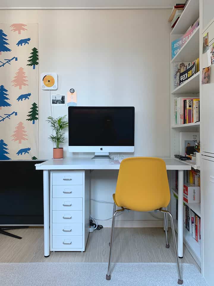 Simple home office study in white and yellow tones featuring a desk with computer and bookshelf in a clean layout