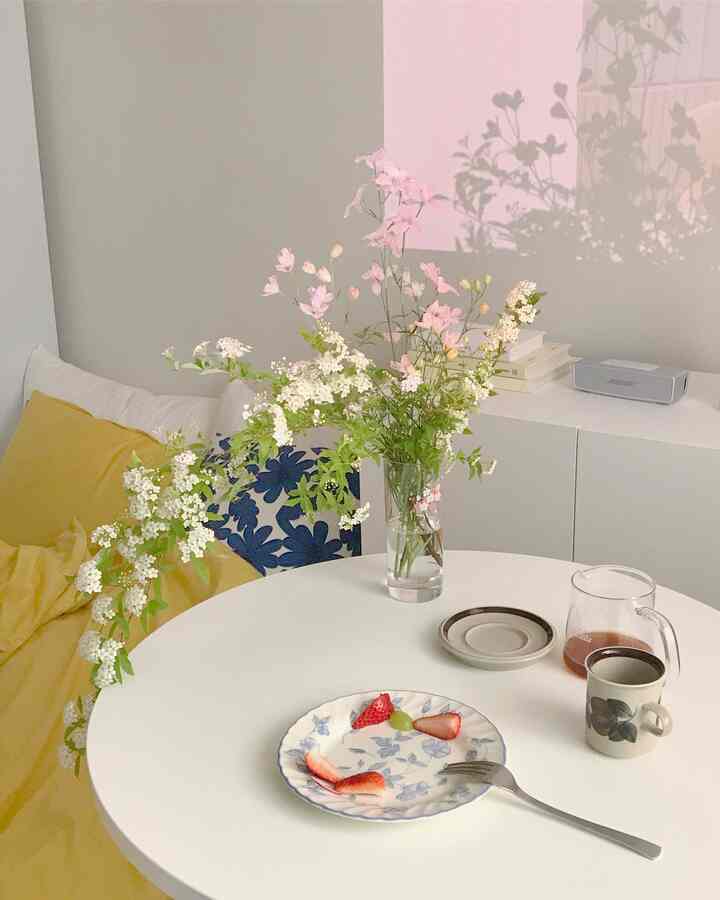Cozy studio apartment living room in white and yellow tones featuring a floral centerpiece and coffee setup reflecting a home cafe vibe