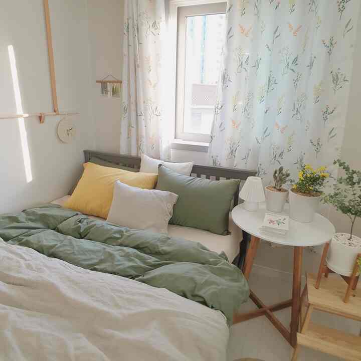 Small bedroom with white walls and wood-toned furniture, featuring floral patterned curtains and green cushions for a spring vibe