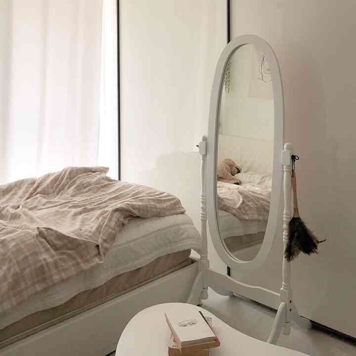Beige and white toned studio bedroom featuring bedding and a full-length mirror with a cozy atmosphere