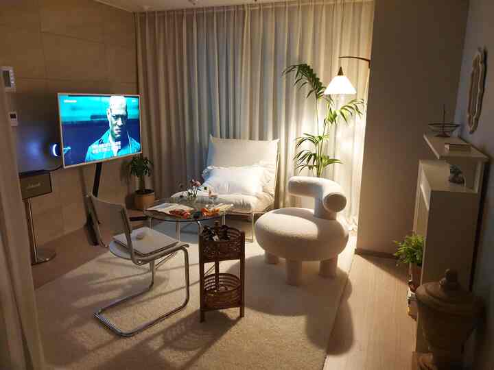 Soft white and natural tone living room featuring comfortable armchairs, wall sconce lighting, and a rattan basket creating a cozy atmosphere