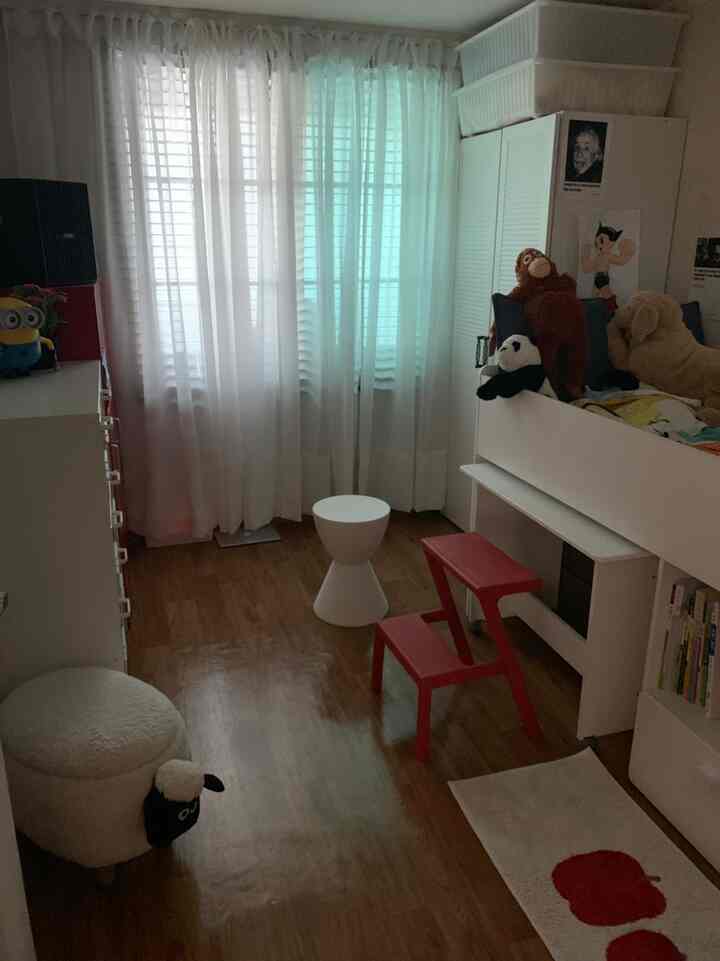 A cozy kids' room in white and wood tones, featuring a kids' bed, desk, stuffed animals, and storage cabinets