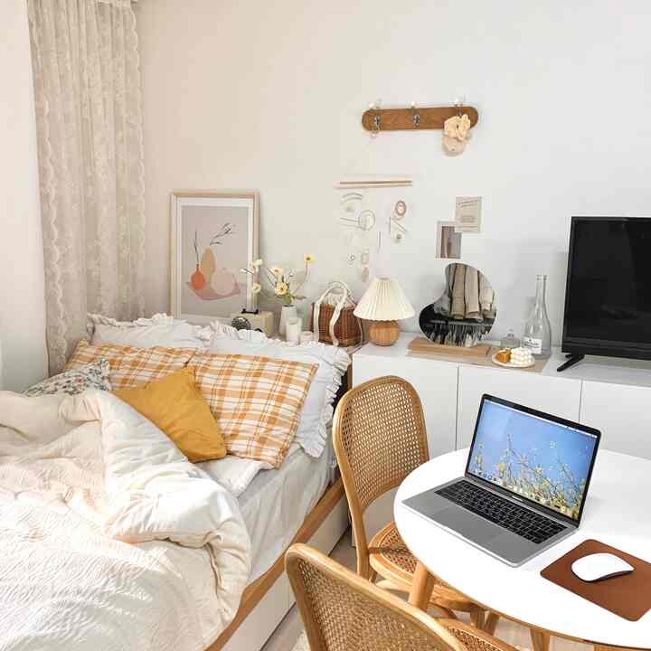 白とナチュラルウッドの色調のワンルーム寝室、丸テーブルと快適な枕カバー、おしゃれなインテリア小物が配された印象的な空間