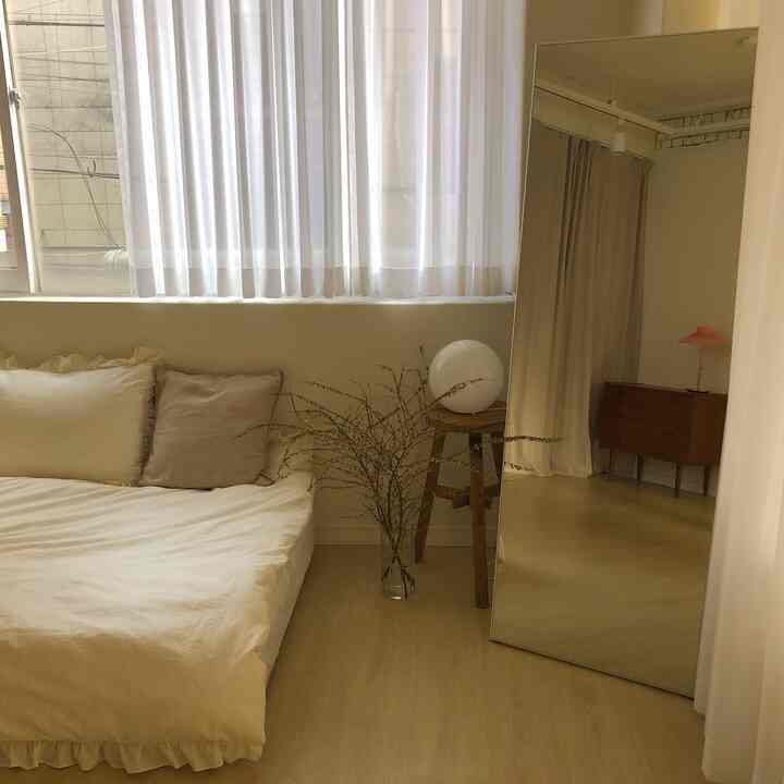 Natural style bedroom in white and beige tones, featuring a low bed, wooden stool, and large floor mirror creating a harmonious atmosphere