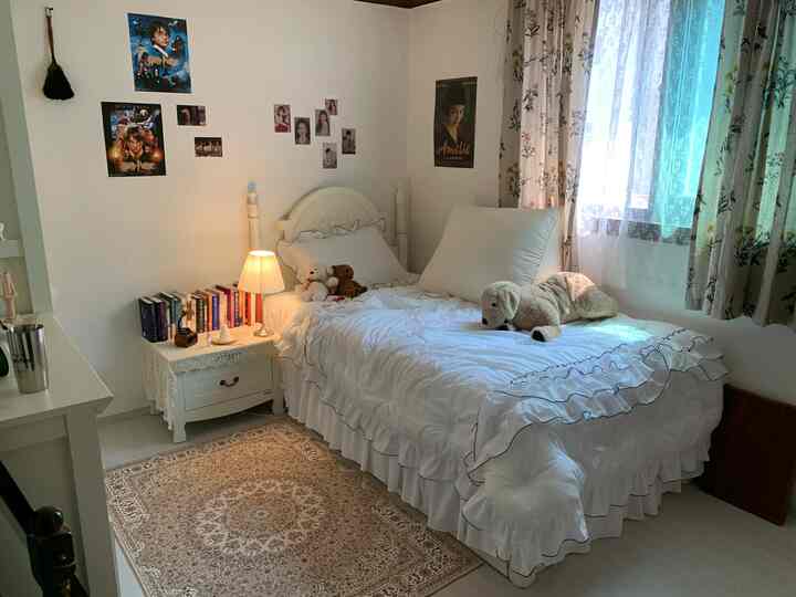 White and natural-toned bedroom featuring a white bed, Persian rug, and decorated posters creating a cozy atmosphere