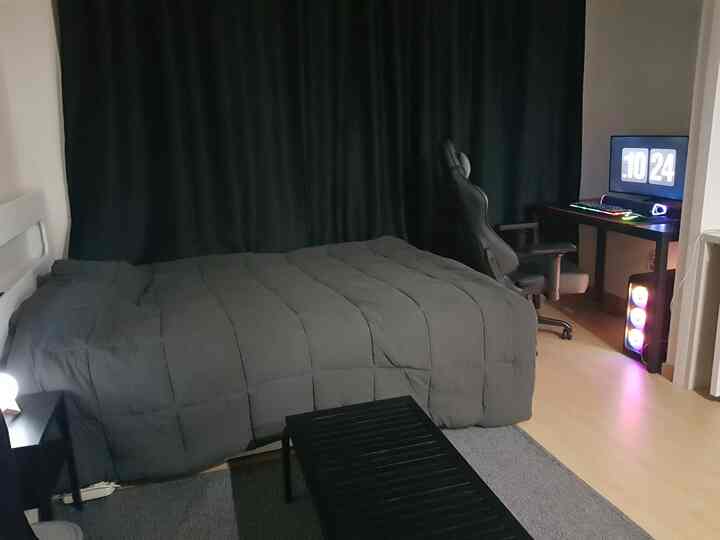 Charcoal and black toned studio bedroom featuring blackout curtains and a gaming chair, creating a modern and calm atmosphere