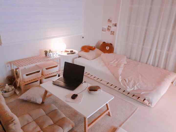 Bright natural-toned small bedroom featuring a wooden bed frame, low desk, curtains, and blinds creating a cozy atmosphere