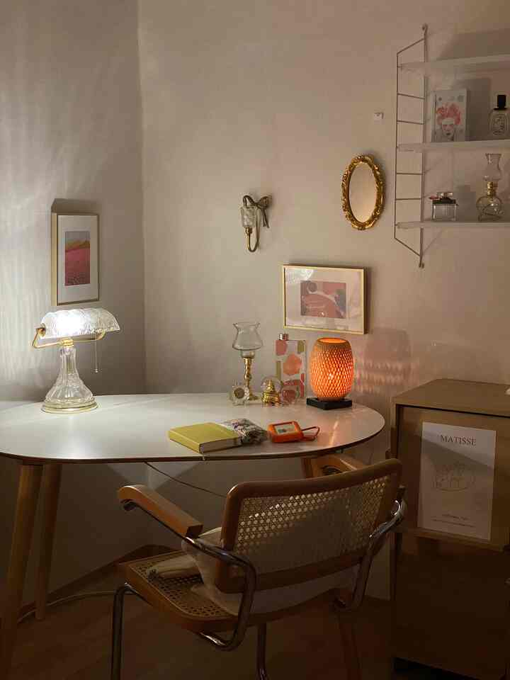 White and wood tone workspace featuring a rattan chair, decorative lamps, and shelves creating a cozy natural atmosphere