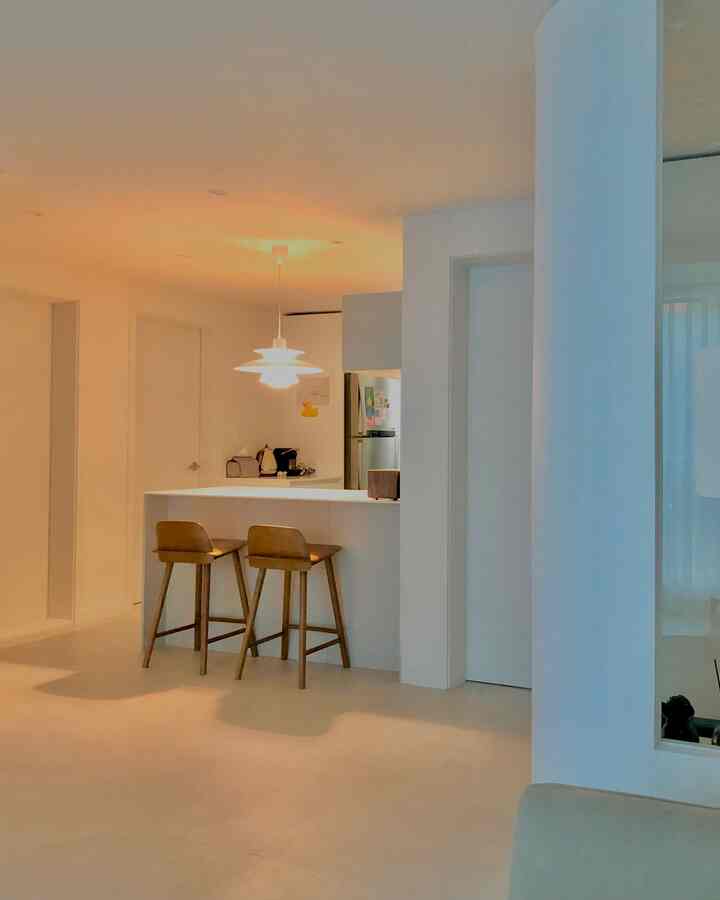 Bright white and light warm gray 20-pyeong apartment kitchen featuring two wooden bar stools and a pendant light, showcasing a clean, spacious interior.
