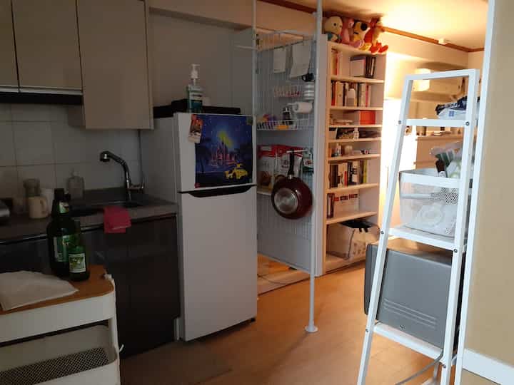 White and natural toned entrance featuring partition, bookshelf, refrigerator, and kitchen cart in a cozy space