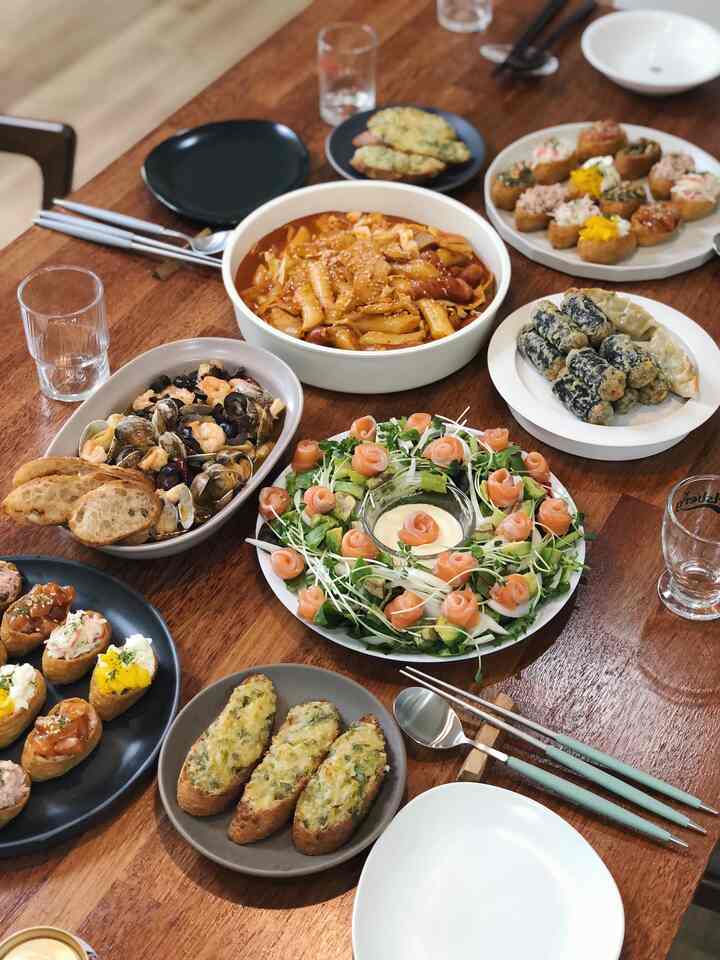 ナチュラルなブラウンウッド調ダイニングテーブルに多様な皿とカトラリーが配置されたホームパーティーの雰囲気