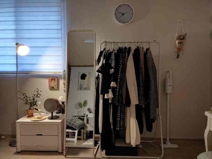 ライトブラウンの床とホワイトのウォークインクローゼット、衣服ラックと全身鏡、照明が配置された整理されたモダンなインテリア