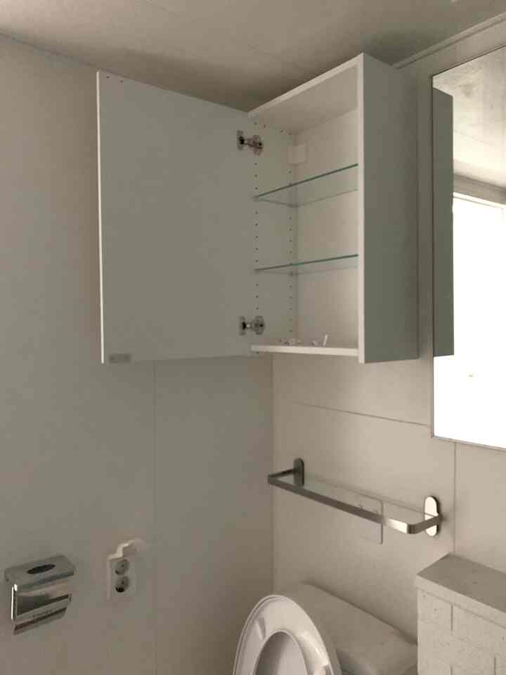 White-toned bathroom featuring a wall-mounted storage cabinet with glass shelves, creating a clean space