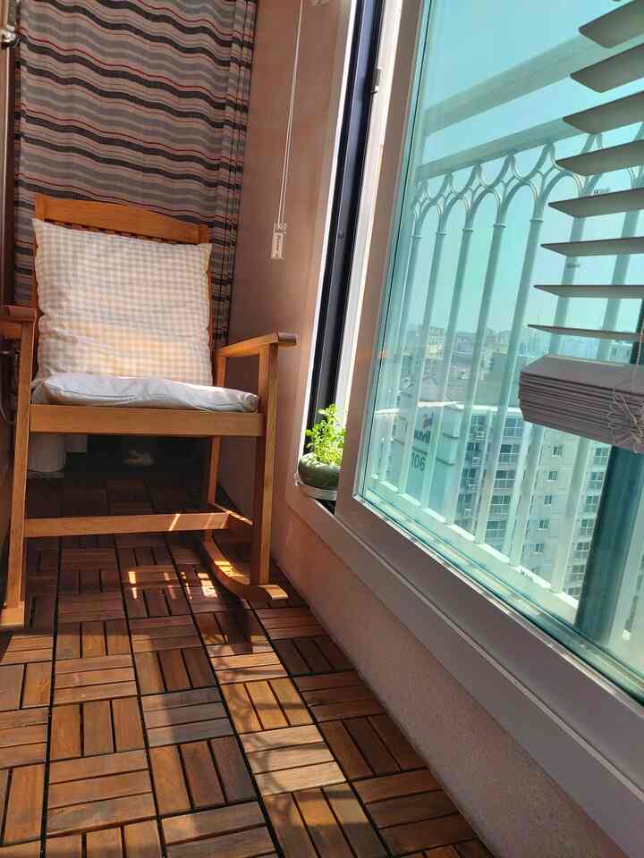 ナチュラルな木目調のバルコニー、チェック柄のクッション付きロッキングチェアと小さな植木が配置された雰囲気のある空間