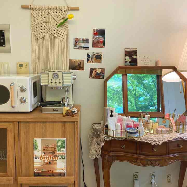 Studio apartment with white walls and wood tone furniture, featuring a vanity and kitchen appliances creating a warm and cozy atmosphere