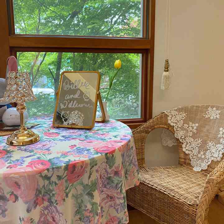 Warm wood tones and floral patterns define this home cafe space featuring a rattan chair and a table with a floral tablecloth, creating a cozy atmosphere