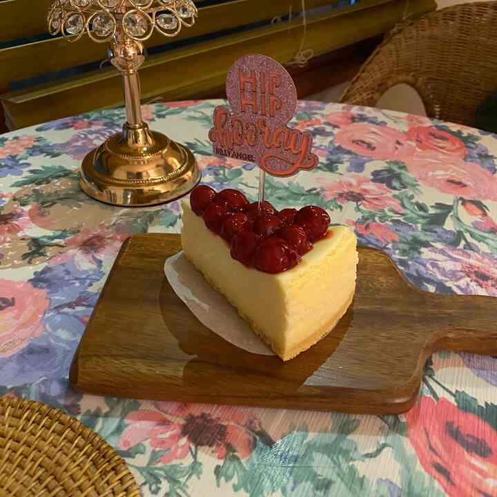 華やかな花柄のテーブルに木製カッティングボードとラタンの丸形ランチョンマットが置かれ、『HIP HIP hooray』の飾り付きケーキのスライスがあるホームパーティー空間