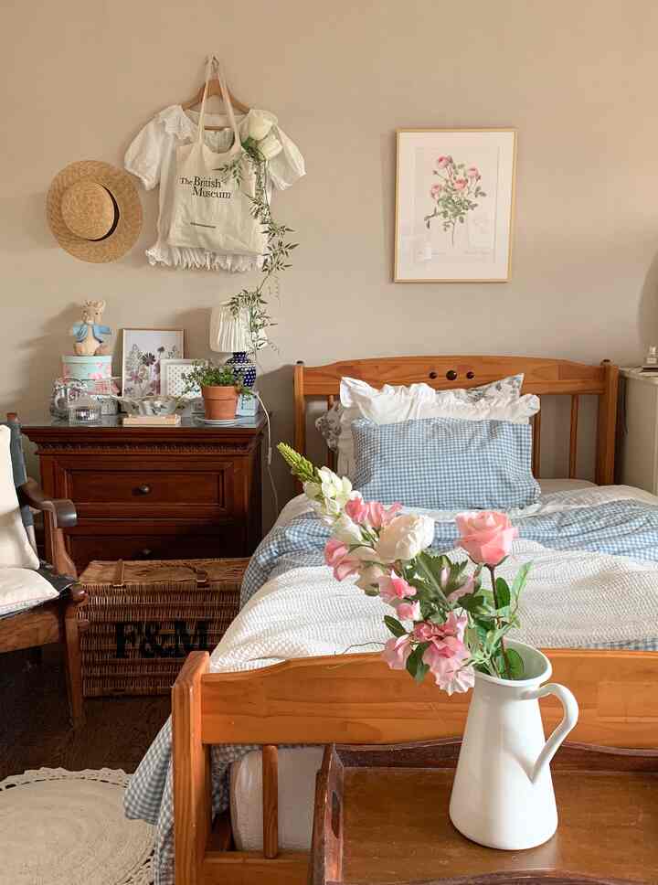 Natural bedroom in warm wood tones featuring blue check bedding, a vase with flowers, and a floral poster creating cozy atmosphere