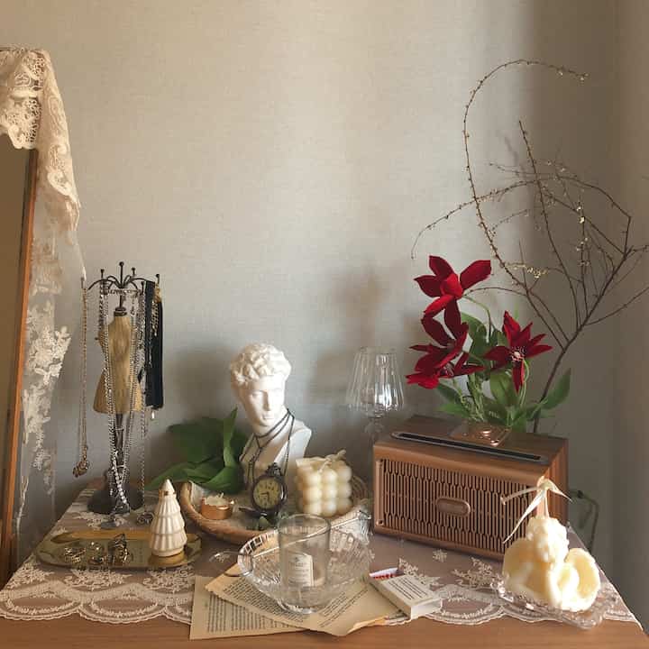 Natural toned room table adorned with lace table runner, white objets, and red floral accents creating an elegant decorative space