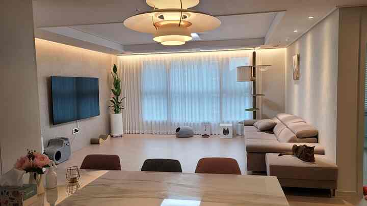 A white and beige toned living room featuring a large sofa, cat tower, and cat houses creating a cozy atmosphere