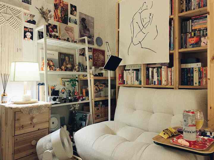 Natural wood tone and white-toned study featuring bookshelves, posters, and a cozy single sofa