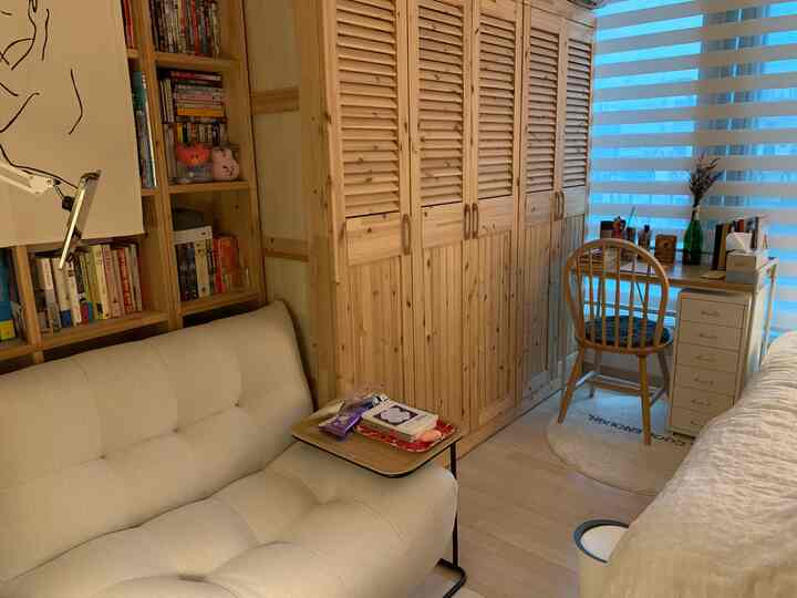 Compact bedroom study in white and wood tones, featuring sofa, bookshelf, and wardrobe in a multifunctional space