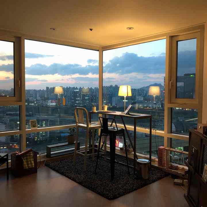 Cozy veranda space in warm natural tones featuring a bar table and stools on a rug by large windows with city view