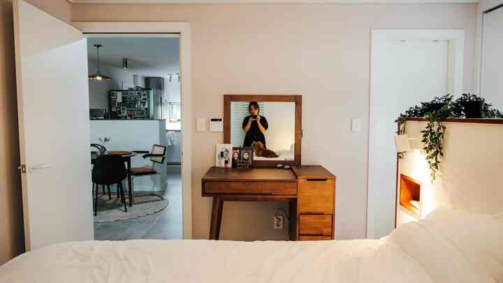 White and brown natural-toned bedroom with wooden vanity and a small pet dog reflected in the mirror, cozy atmosphere