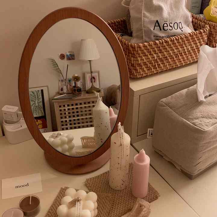 Cozy natural-style living area with warm beige and wood tones featuring an oval wooden mirror, rattan basket, and assorted candles