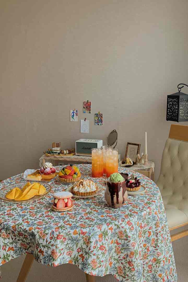 Light beige-walled dining room featuring a white floral tablecloth with desserts and drinks set for a cozy home cafe atmosphere