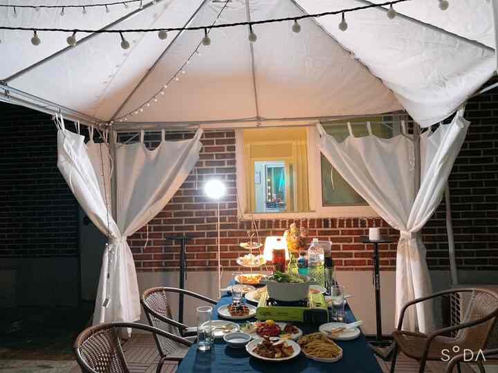 Cozy rooftop party setup under white canopy featuring rattan chairs and a table filled with food and drinks