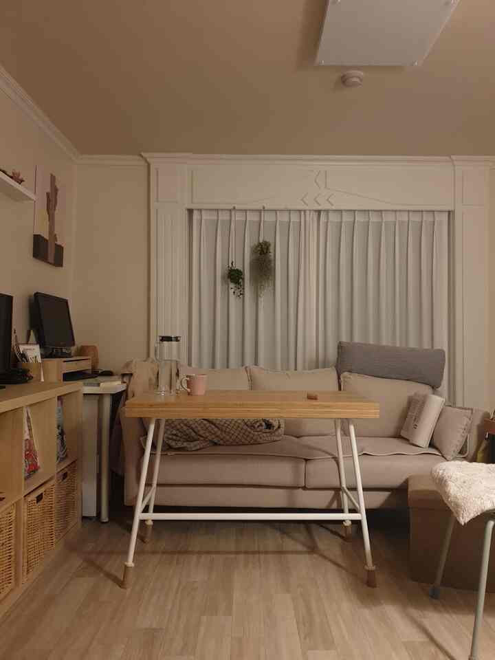 Natural tone living room with warm wood tones and beige sofa, white curtains in background creating cozy atmosphere
