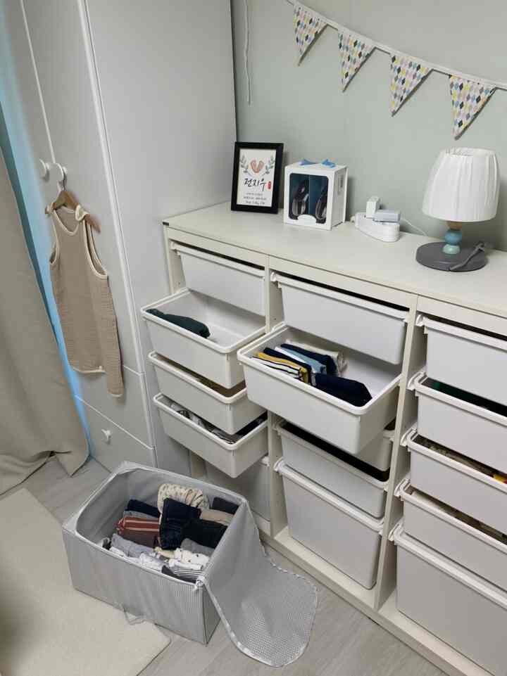 白を基調とした子供部屋、複数の収納棚と整頓された赤ちゃんの服が配置された雰囲気のある空間