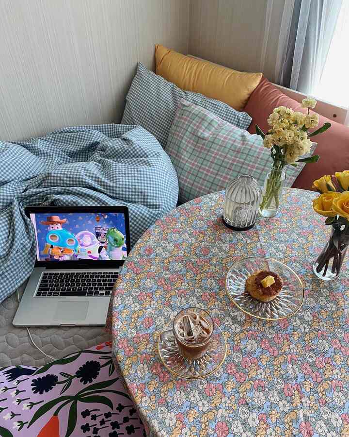 Pastel tone floral-patterned small studio bedroom featuring a round table set for home cafe with cushions and natural light
