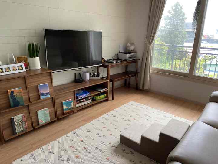 Beige and wood tone living room featuring sofa, pet steps, TV stand, and curtains in a cozy atmosphere